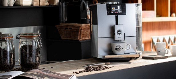 une machine à expresso moderne sur un comptoir de cuisine avec une tasse à café sous le distributeur. deux pots de grains de café se trouvent à proximité.