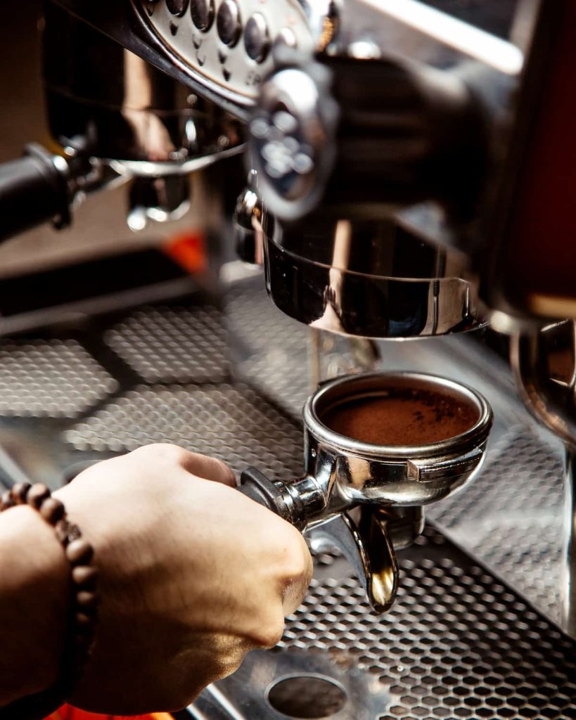 une main tenant un porte filtre inséré dans une machine à expresso.