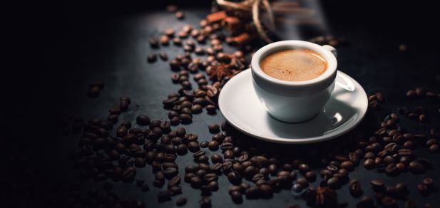 une tasse d'espresso blanche sur une soucoupe est entourée de grains de café éparpillés sur une surface sombre.