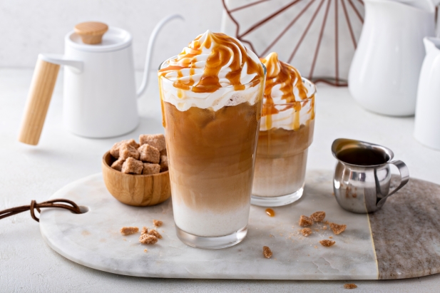 deux boissons glacées au caramel macchiato garnies de crème fouettée et d'un filet de caramel, placées sur une planche en marbre entourée d'un petit pichet, d'un bol de cubes de cassonade et d'une théière blanche.