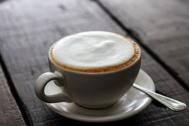 une tasse en céramique de cappuccino avec du lait mousseux sur une soucoupe assortie, posée sur une table en bois. une petite cuillère repose sur la soucoupe.