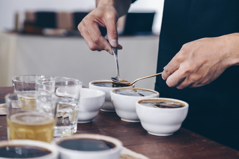 personne effectuant une séance de dégustation de café avec plusieurs bols et verres sur une table.