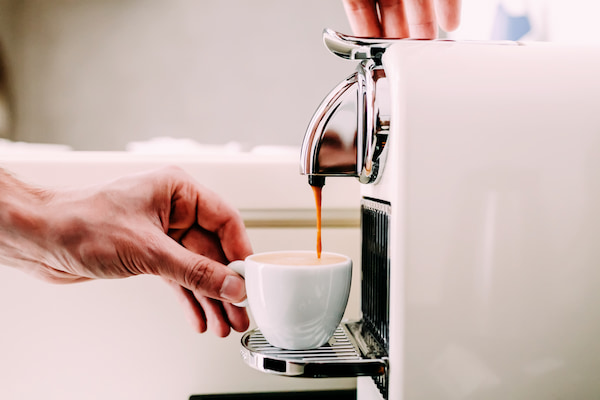 une main tient une petite tasse sous une machine à expresso, avec du café coulant du bec.