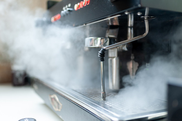 gros plan d'une machine à café avec de la vapeur sortant de la buse à vapeur, indiquant son fonctionnement.