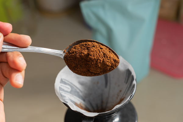 main tenant une cuillerée de café moulu sur un filtre en papier dans une cafetière.